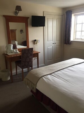 A hotel room with a bed, a desk with a chair, a television, a mirror, and a window with curtains.