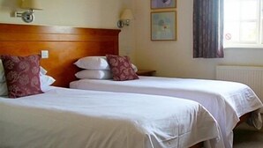 A hotel room with two beds, each with white bedding and multiple pillows. There are wall-mounted lamps and two framed pictures on the wall. - The Crown Inn (Swindon)