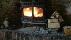 A wood-burning stove with logs and a brick fireplace. - The Crown Inn (Swindon)