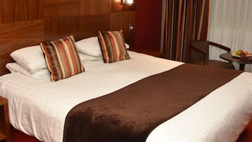 A large bed with multiple pillows, a wooden headboard, a red carpet, a small table with fruit, and a painting on the wall.