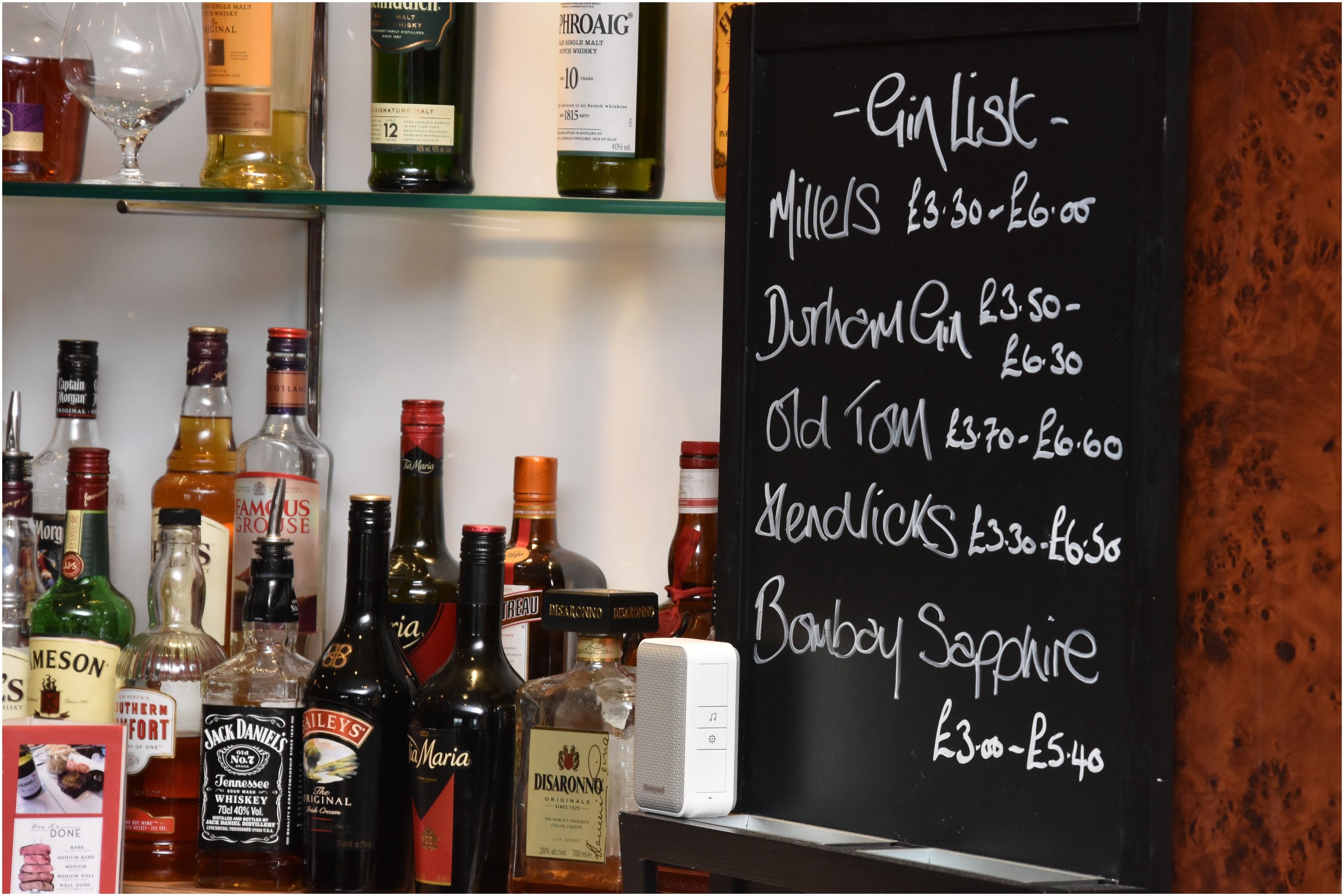 Zona de bar con un menú en pizarra que enumera diversas bebidas alcohólicas y sus precios.