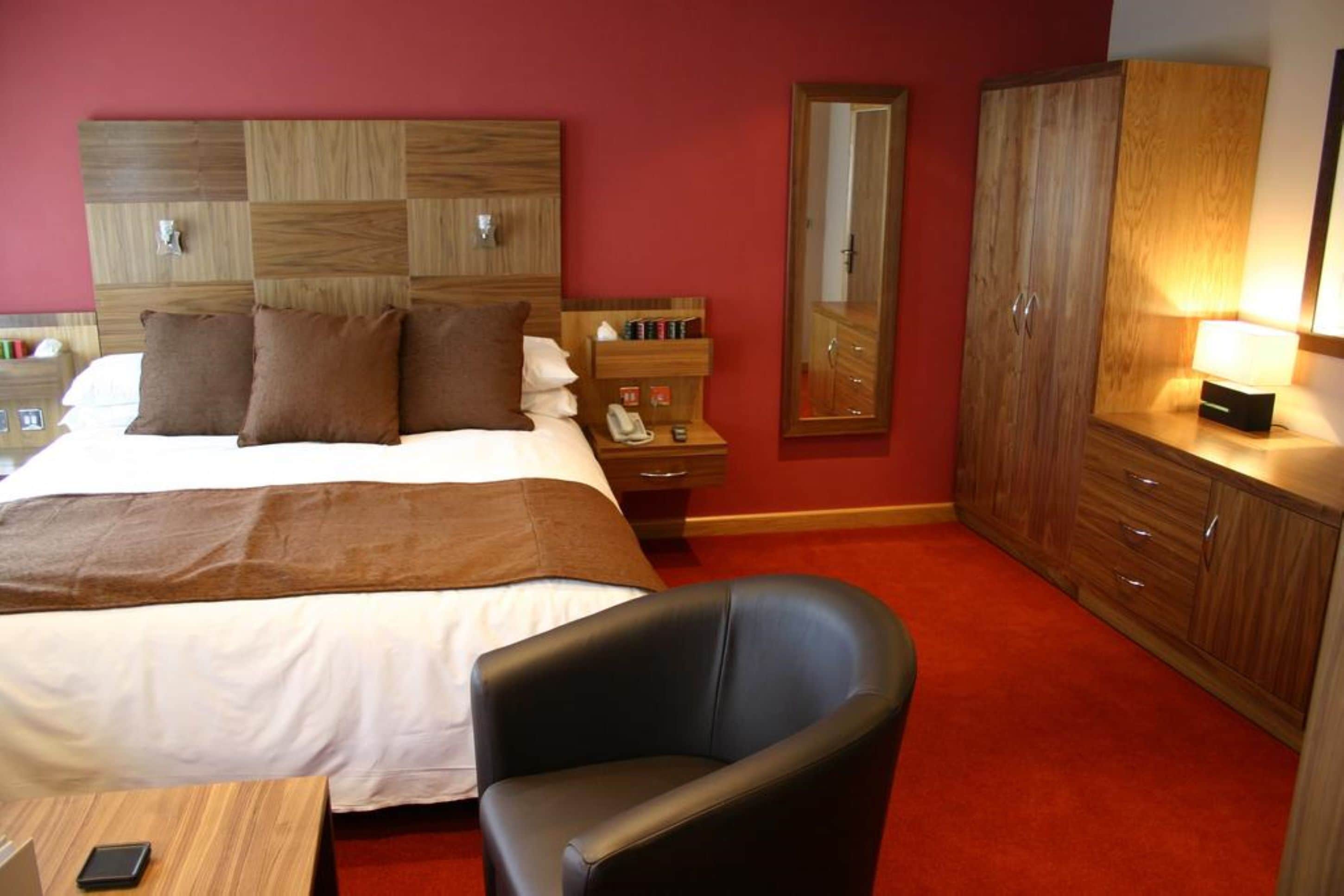 Habitación de hotel con una cama grande, cabecera de madera, escritorio con silla, armario y espejo.