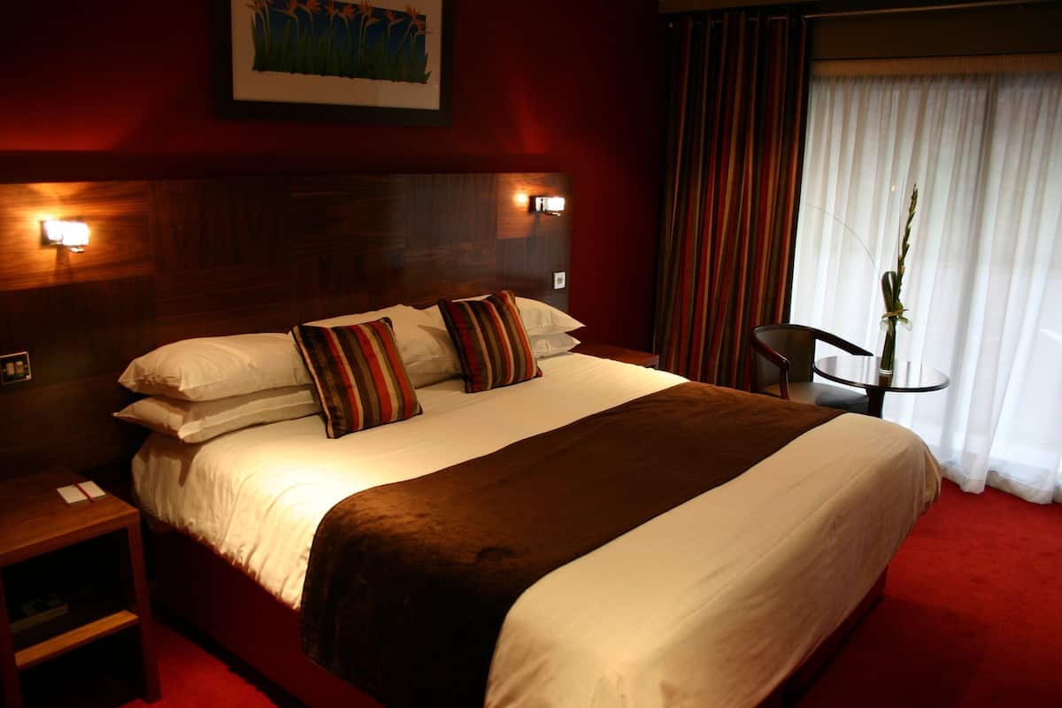 Een hotelkamer met een groot bed, twee bedlampjes, een nachtkastje, een stoel en een raam met gordijnen.
