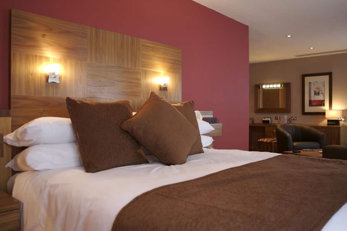 Een hotelkamer met een groot bed, twee wandlampen, een houten hoofdeinde, een bureau en een stoel.
