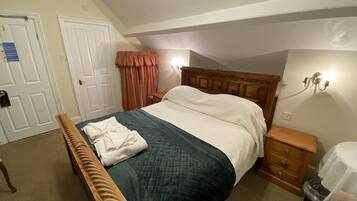 Une chambre à coucher comprenant un lit, une tête de lit en bois, une table de chevet, un banc, une lampe fixée au mur et une porte.