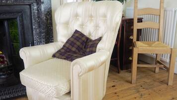 A white leather armchair with a plaid pillow, a wooden chair, a vase of white flowers, and a fireplace with decorative glass panels.