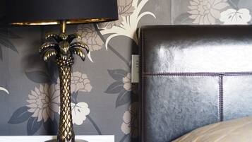 Una cama con cabecera negra, una lámpara decorativa con diseño de palmera y un estampado floral en el papel tapiz.