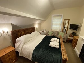 A bedroom with a large bed, a wooden dresser, a small table with a lamp, a TV, and a window with curtains. - Old Manse Hotel (Pickering)