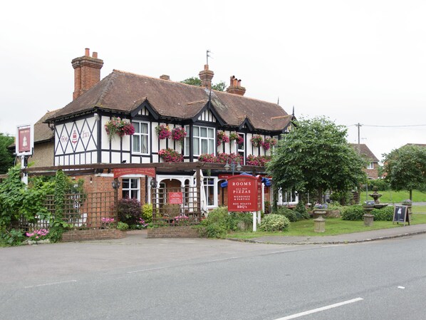Un bâtiment traditionnel de style Tudor, orné d’une enseigne publicitaire annonçant la location de chambres, la vente de pizzas à toute heure, l’organisation de mariages, de fêtes et de barbecues.