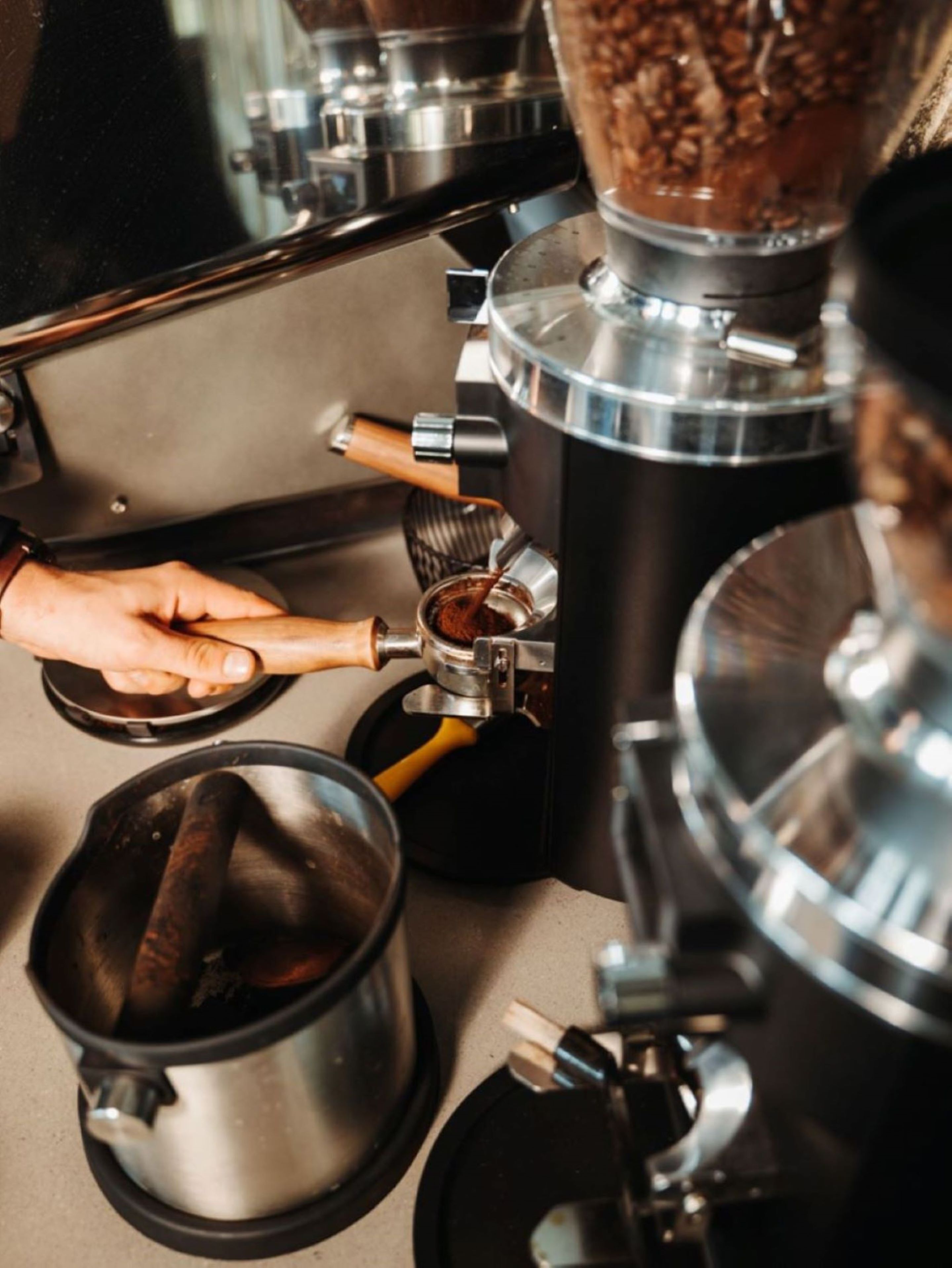 A coffee machine with a hand operating it, a grinder, and a pot.