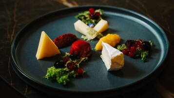 Una mesa de mármol oscuro con un plato azul que contiene diversos quesos y frutas.