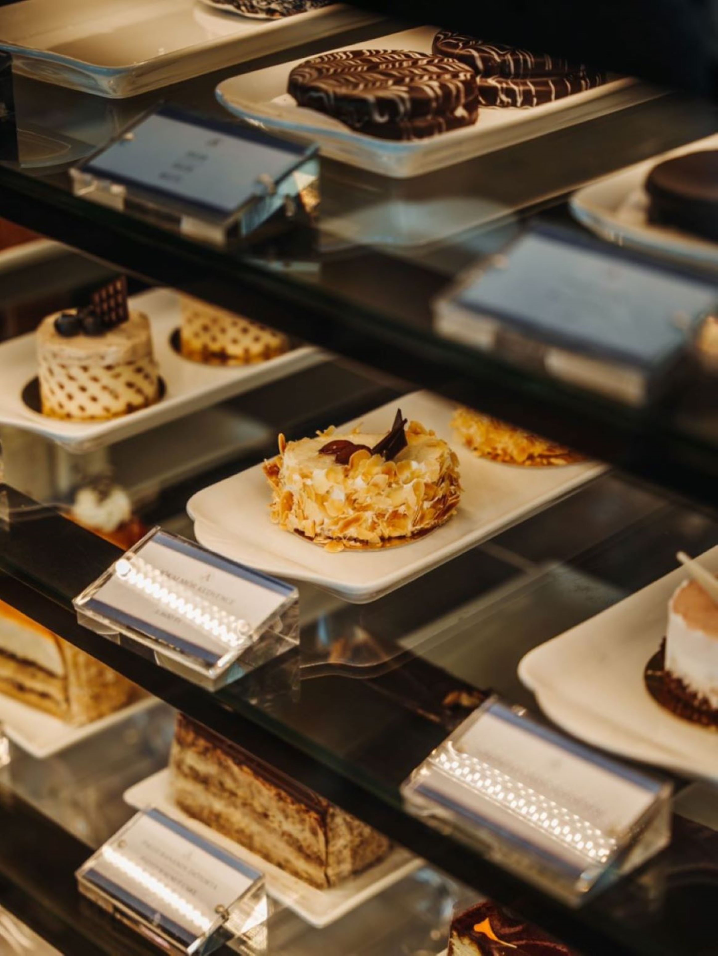 Una vitrina con diversos postres, entre ellos pasteles y bollería, dispuestos sobre platos blancos.