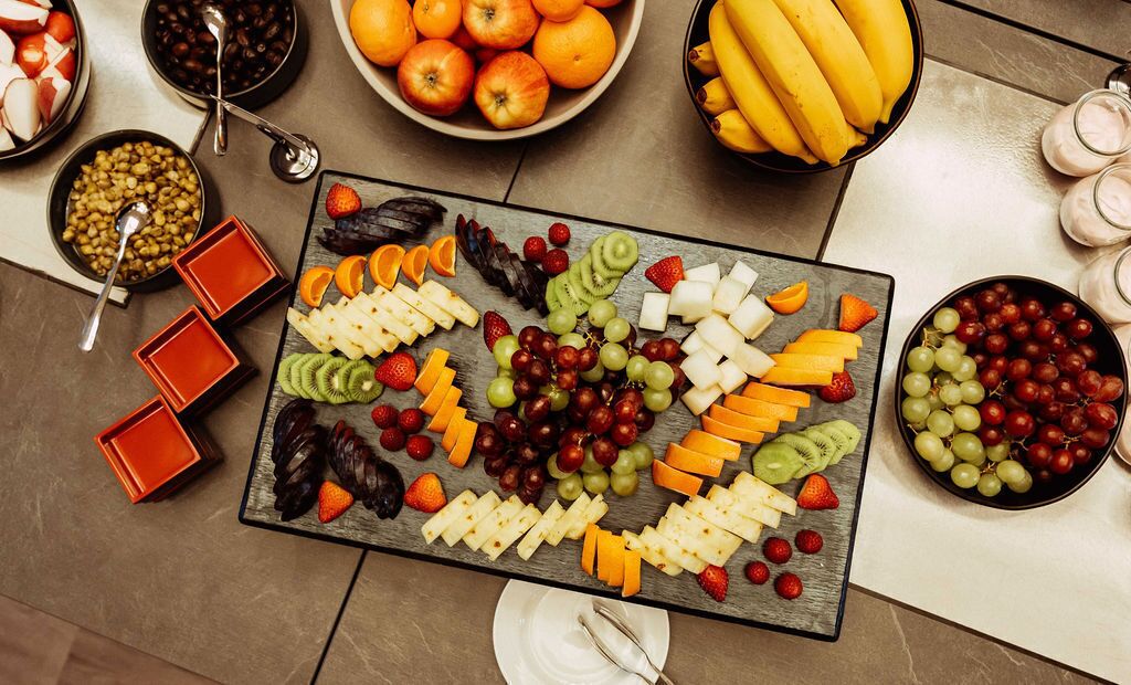 A table with various fruits and cheeses arranged for a buffet.