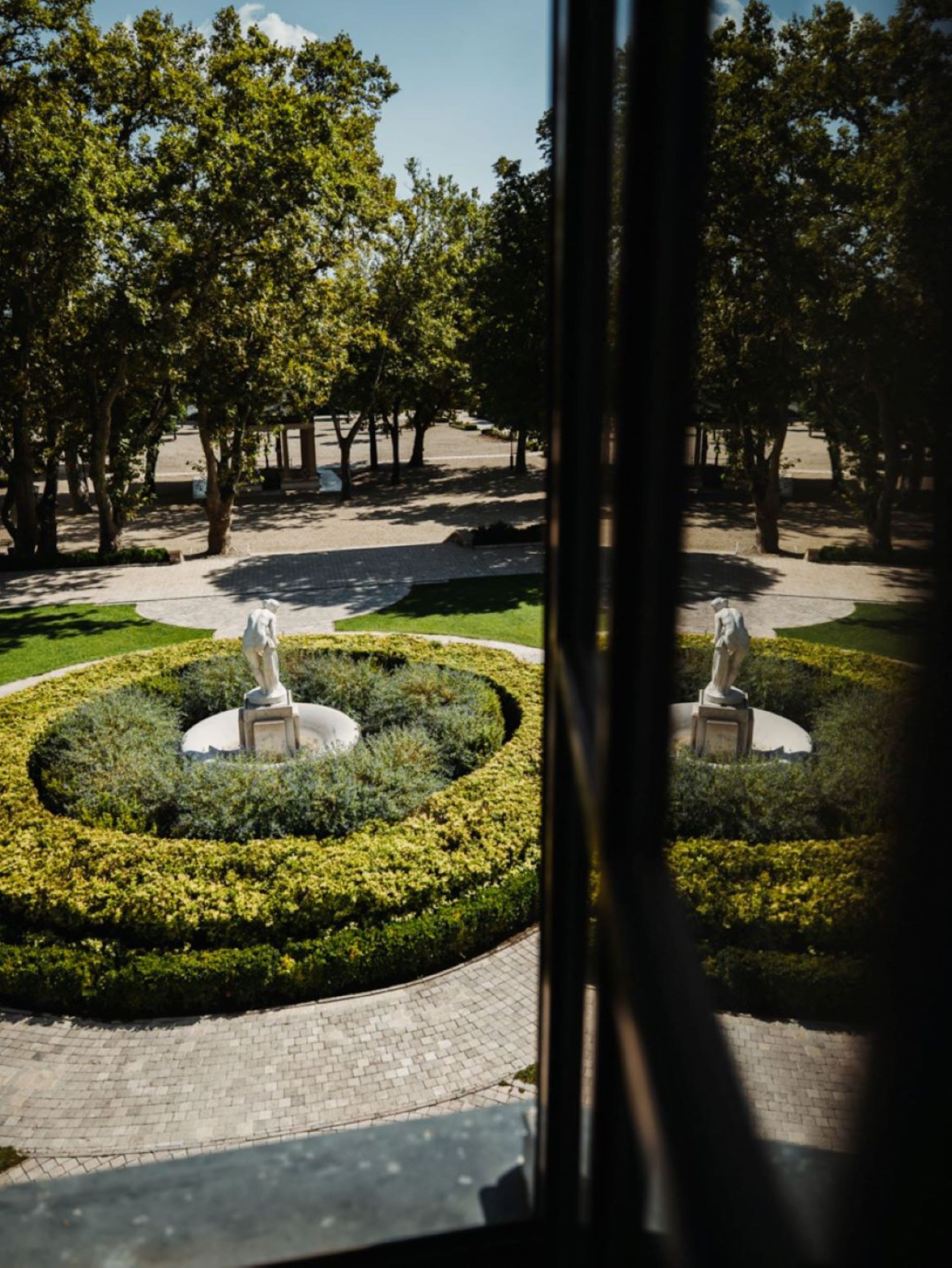 A circular garden with statues, surrounded by a paved walkway and trees.