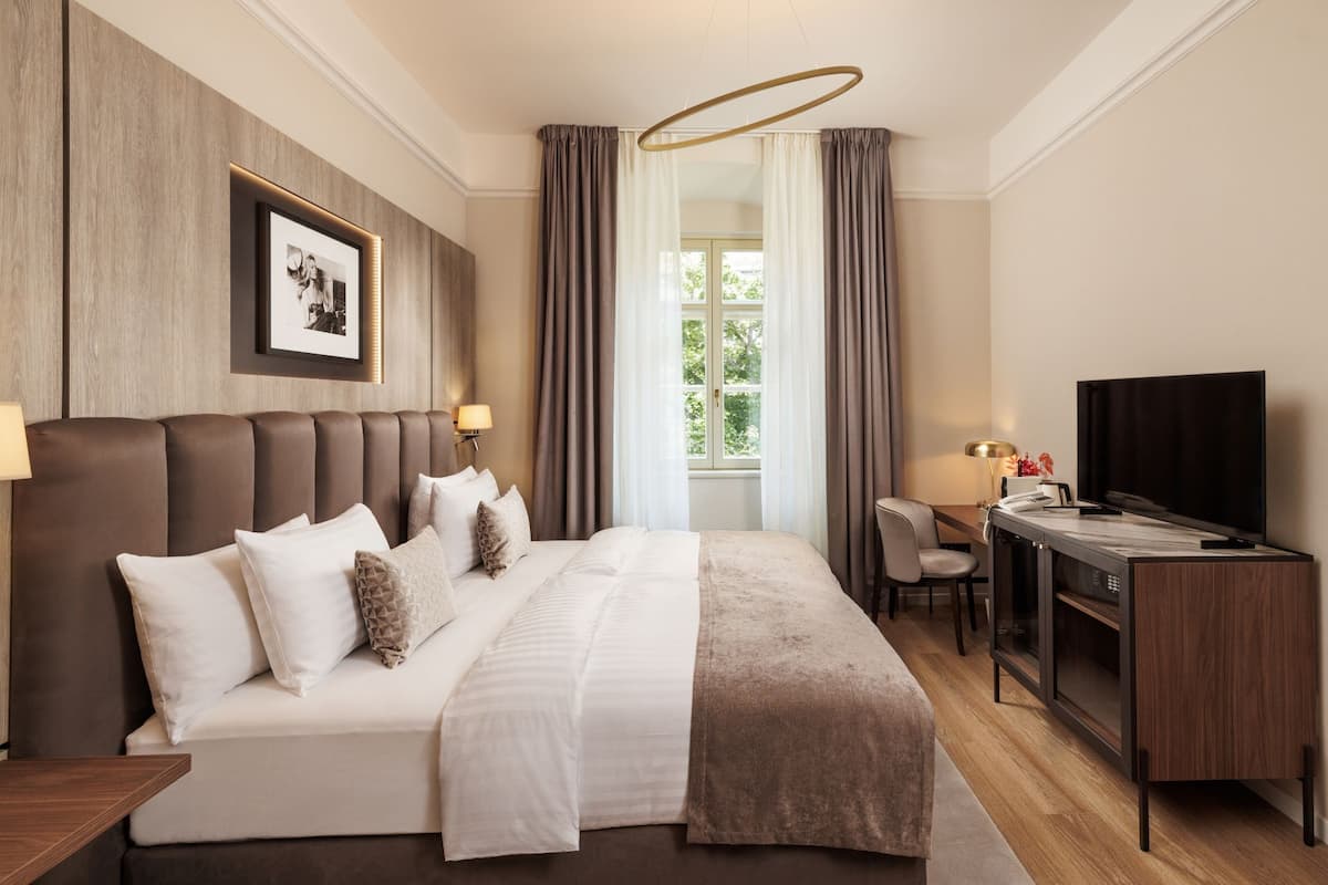 A hotel room with a large bed, a desk with a television, and a window with curtains.