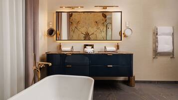 A modern bathroom with a freestanding bathtub, dark blue vanity with gold fixtures, and a large mirror above the sink.