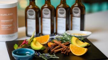 A tray with sliced avocado, orange, cinnamon sticks, and herbs, alongside bottles of Kurland massage lotion and a blue bowl.
