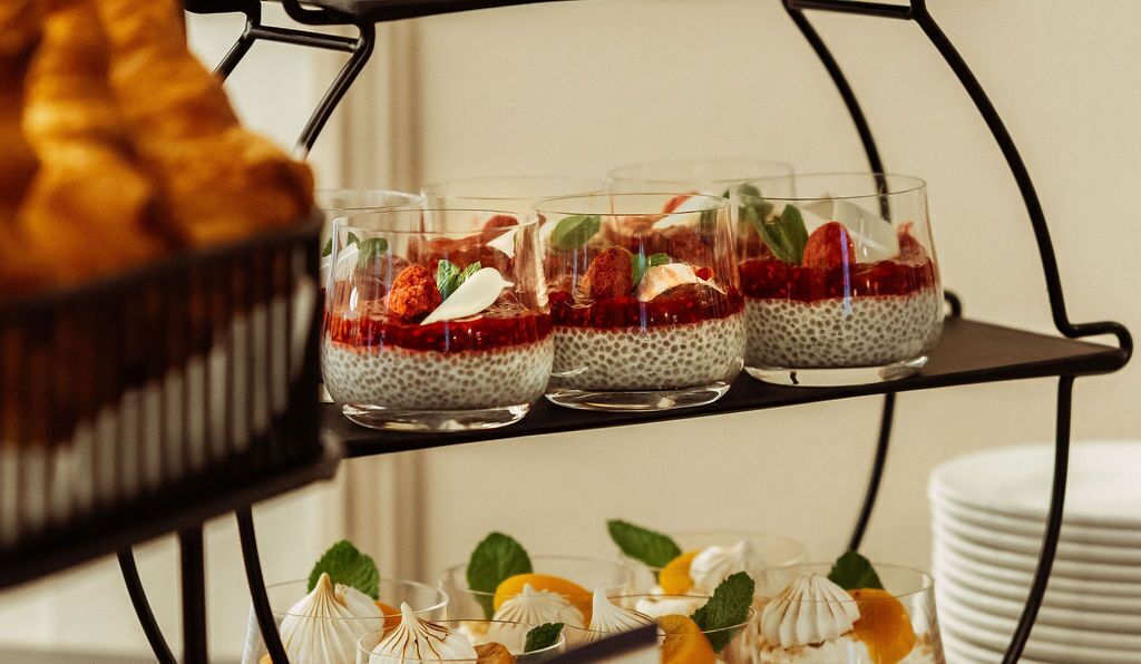 Three glasses of chia pudding with strawberries and mint leaves on a black metal stand.
