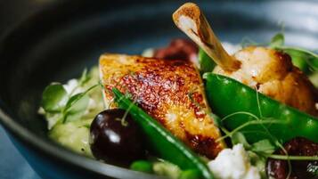 A dish with a piece of grilled fish, green vegetables, and a small piece of bread.