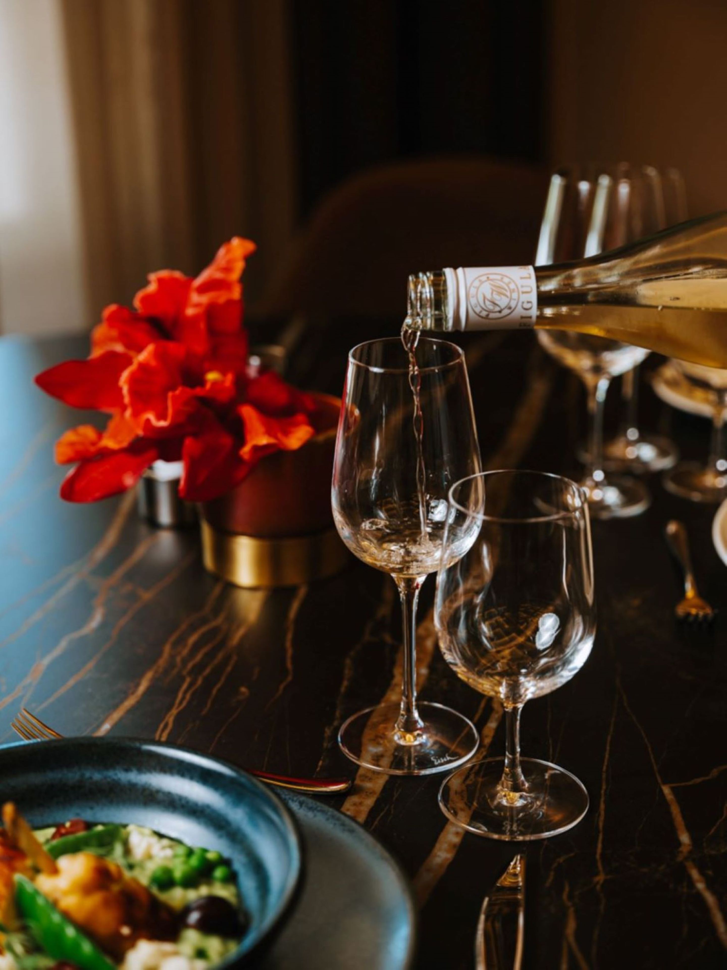 A bottle of champagne being poured into two glasses on a marble table.