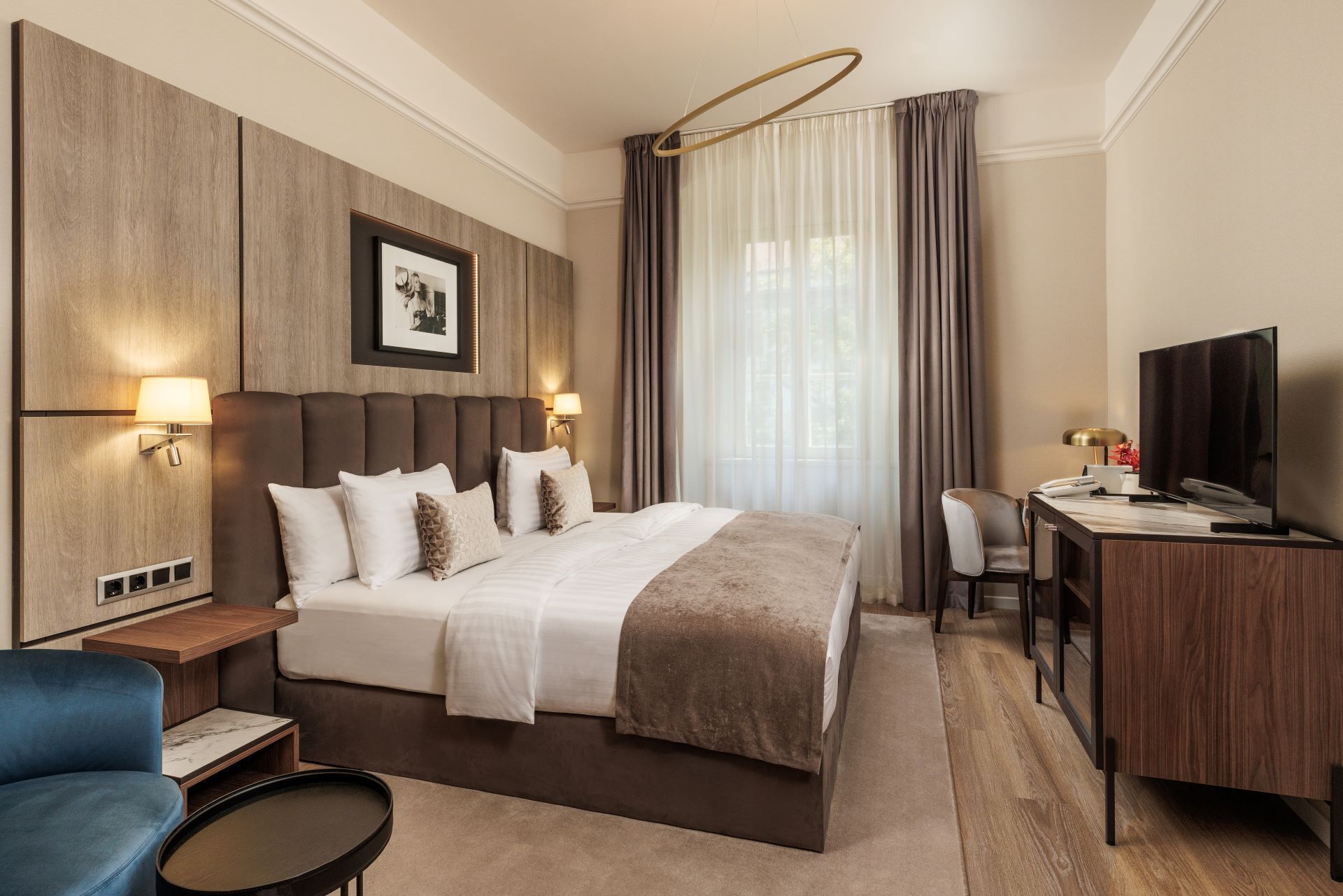 Habitación de hotel con una cama grande, un escritorio con televisor, una silla y una mesita.