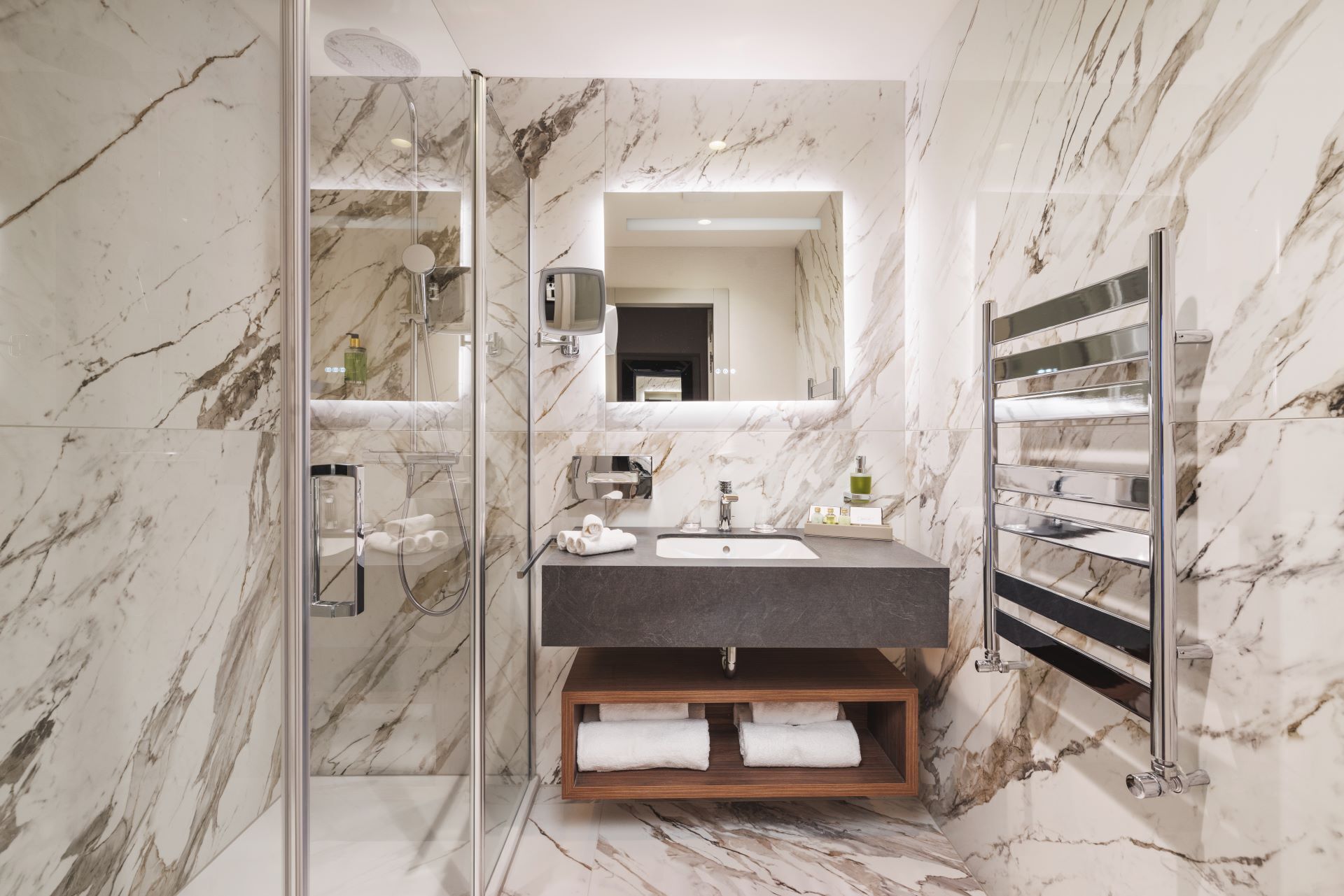 Une salle de bain moderne dotée d’une douche à parois de verre, d’un mur recouvert de carreaux de marbre, d’un lavabo encastré et d’un porte-serviettes.
