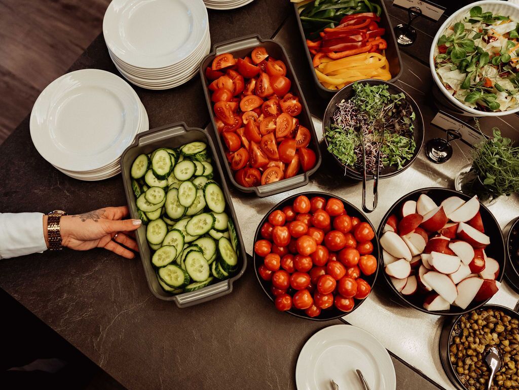 A buffet table with various food items including sliced cucumbers, cherry tomatoes, bell peppers, and a salad.