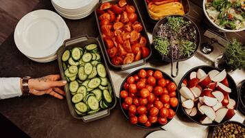 A buffet table with various food items including sliced cucumbers, cherry tomatoes, bell peppers, and a salad.