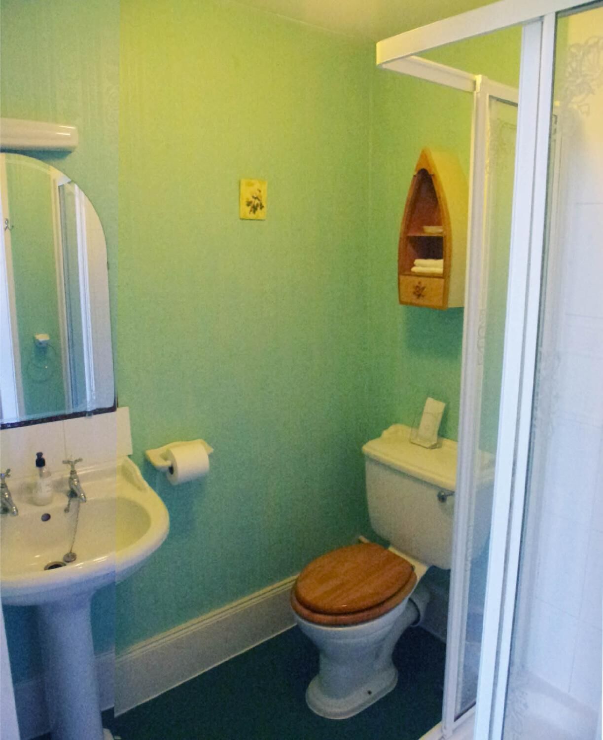 A bathroom with a toilet, sink, and a small shelf above the toilet.