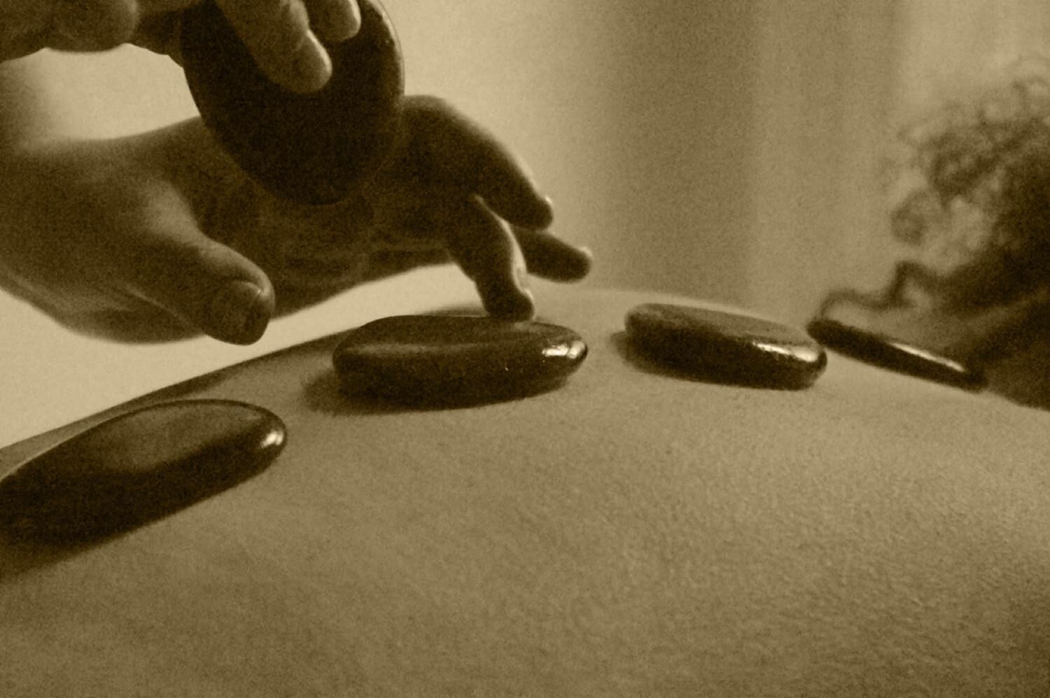 A hand placing a stone on a flat surface with other stones and a knife nearby.