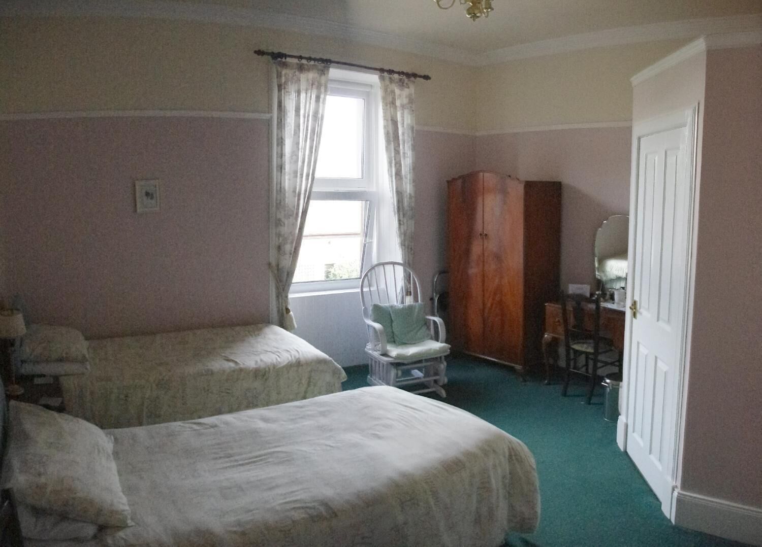 A bedroom with two single beds, a wooden wardrobe, a chair, and a desk.