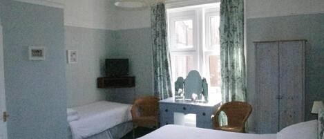 A room with two beds, a desk with a mirror, a television, and a wardrobe.