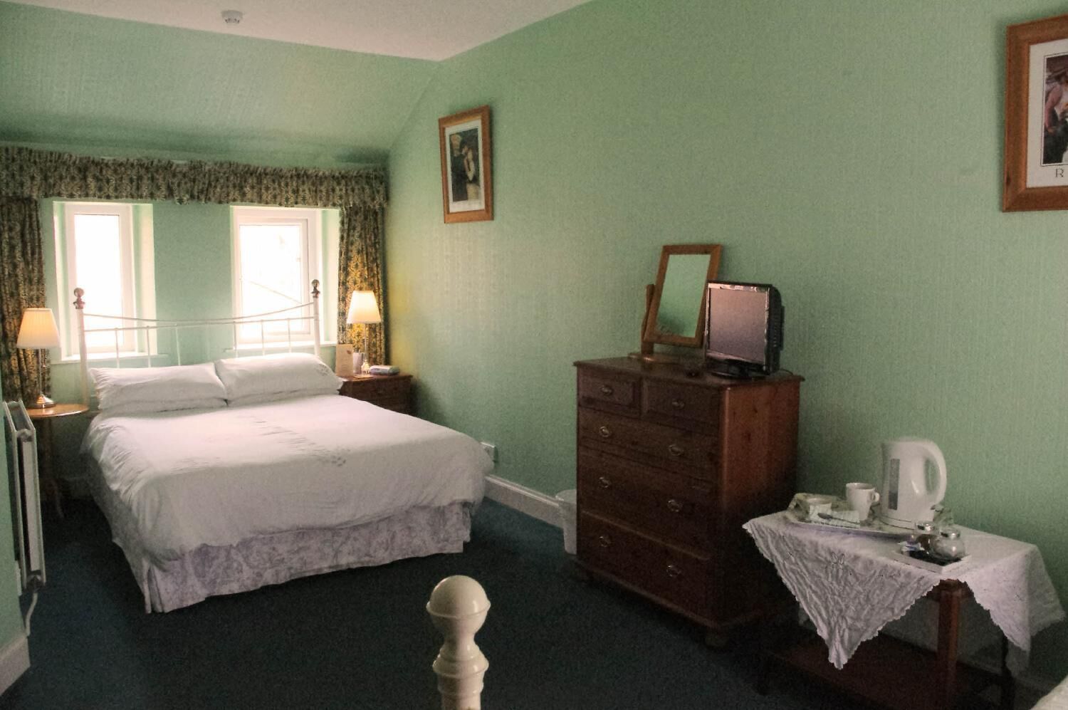 Une chambre à coucher avec un lit, une commode et une table de chevet sur laquelle se trouvent une lampe et une tasse.