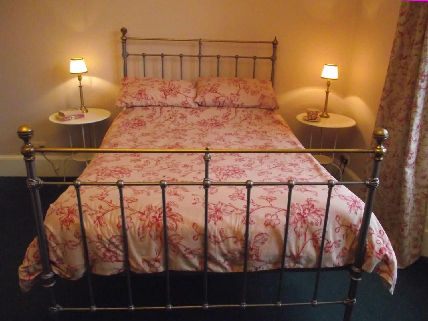A double bed with a floral bedspread and two bedside lamps.
