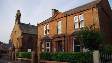 A two-story brick building with a traditional design, featuring a prominent arched window on the ground floor and a symmetrical facade.