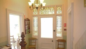 A hallway with a wooden floor, a chandelier, and a door with stained glass panels. - The Old Rectory (Annan)