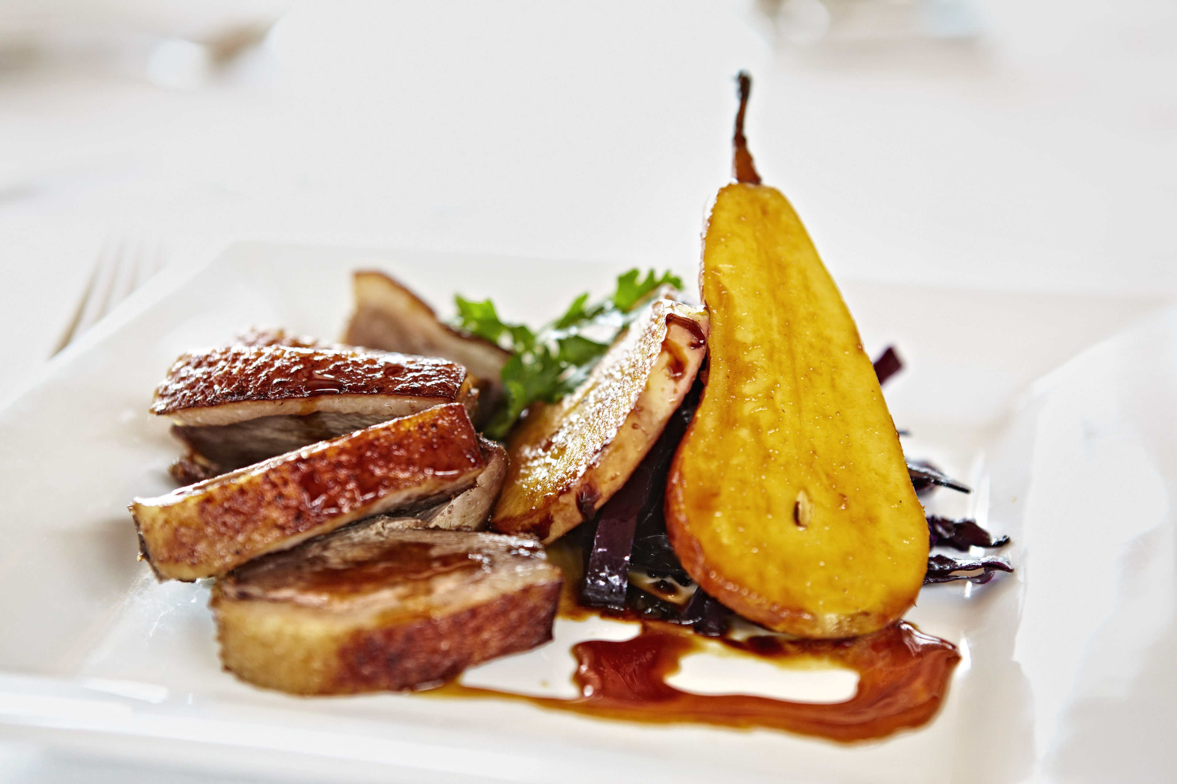 A plate of food with slices of meat, a pear, and some greens.
