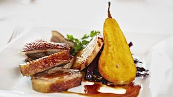 Um prato de comida com fatias de carne, uma pêra e alguns vegetais.