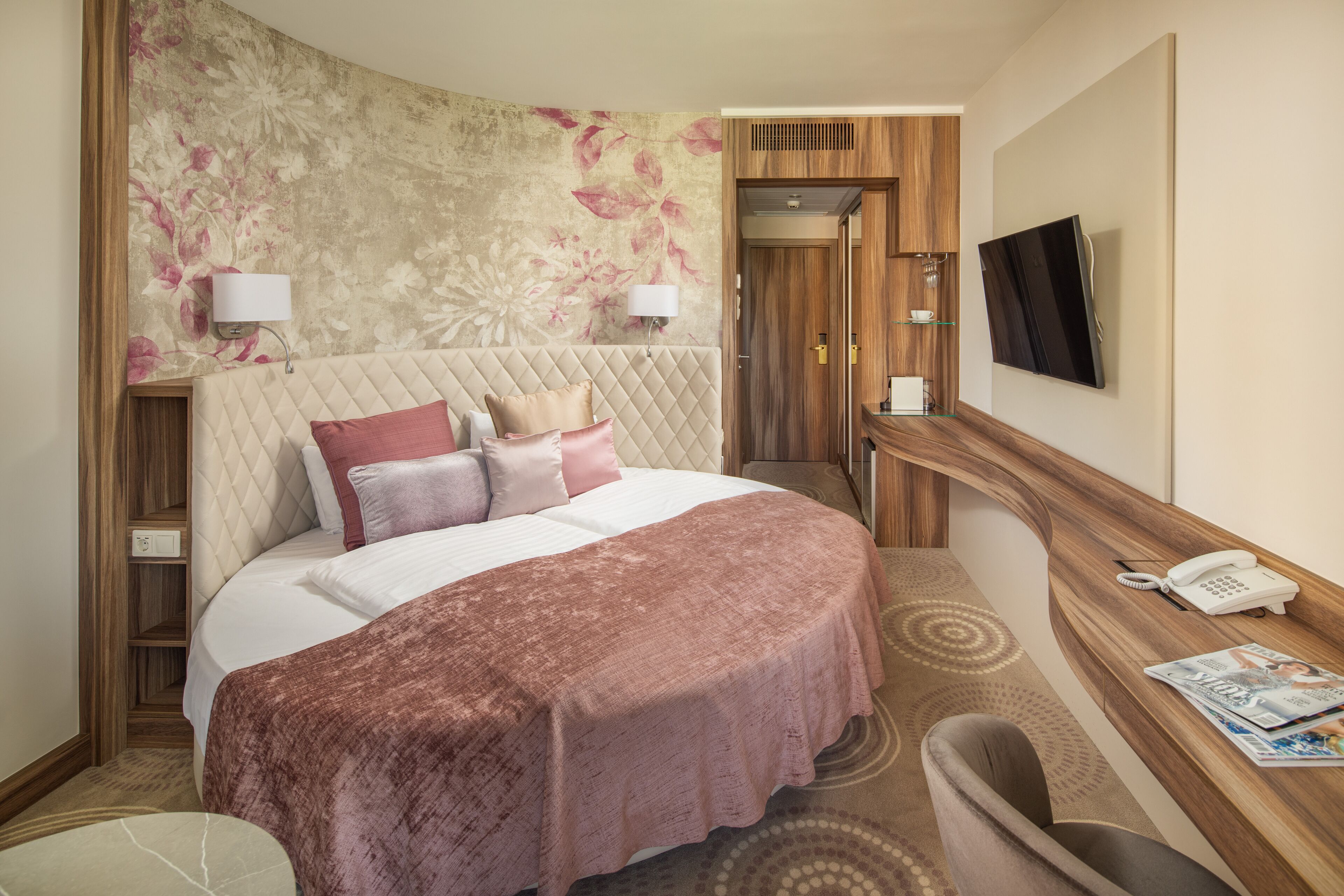 A hotel room with a large bed, a desk with a telephone, and a television on the wall.