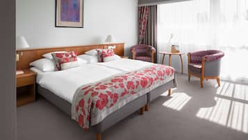 A hotel room with a large bed, two chairs, a small table, and a window with curtains.