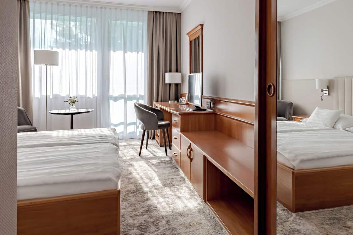 Une chambre d’hôtel avec deux lits, un bureau, une chaise, une télévision et un tableau au mur.