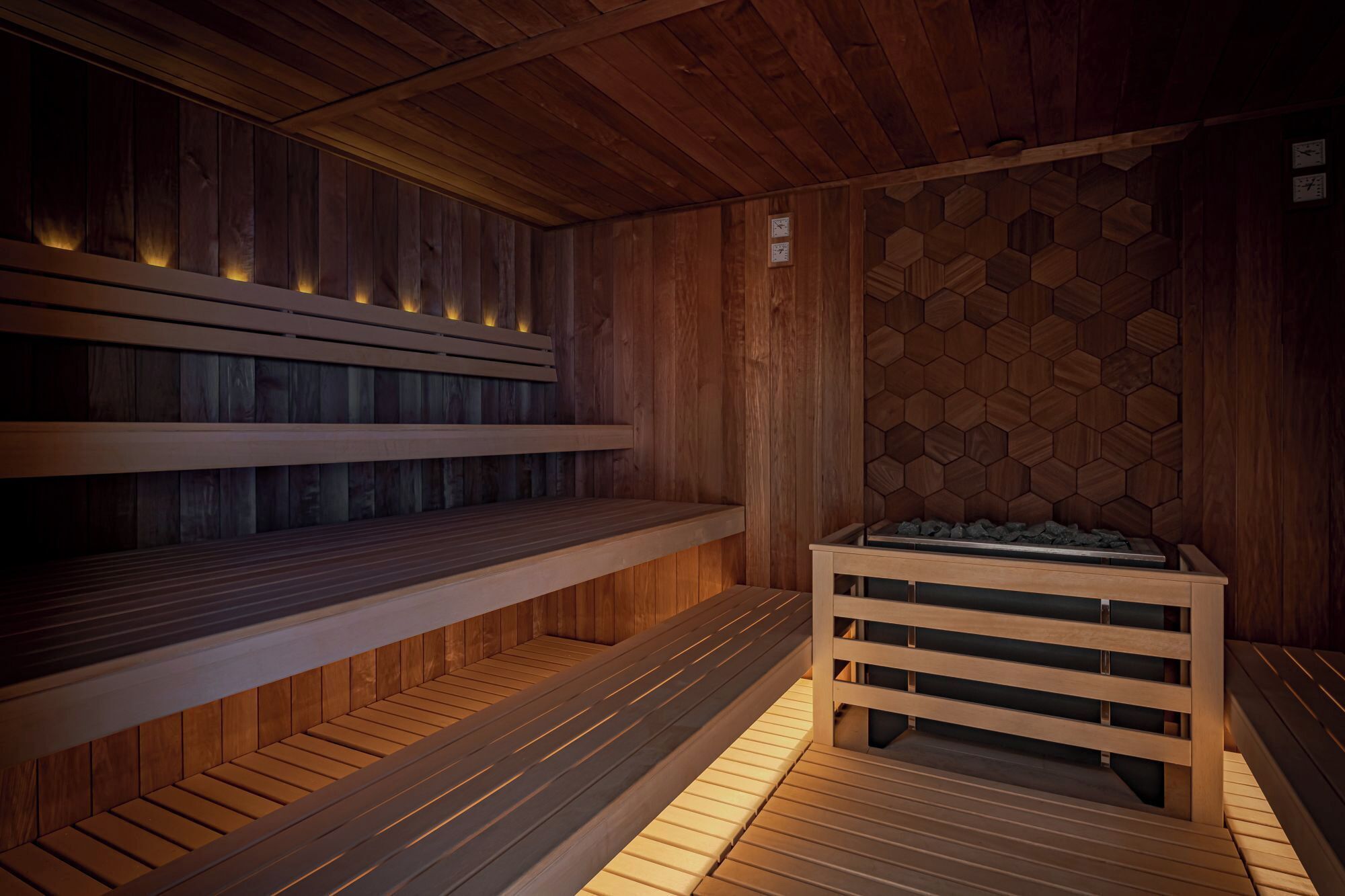 A sauna room with wooden benches and a hexagonal patterned wall.