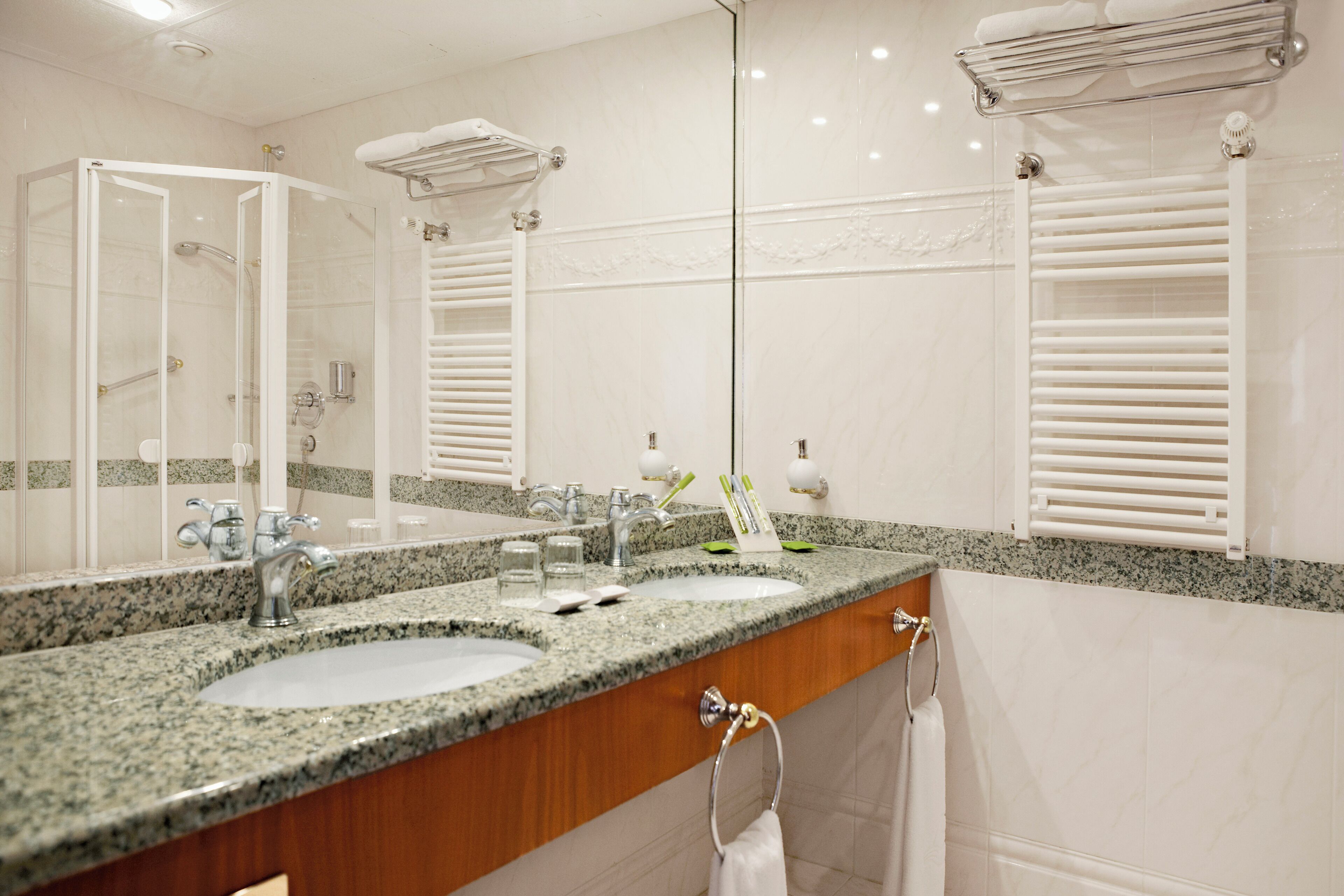 A bathroom with a granite countertop, two sinks, a mirror, and a towel rack.