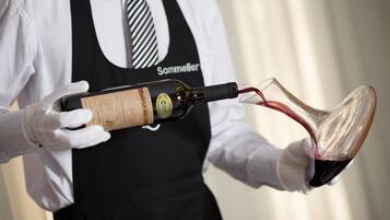 Una persona con camisa blanca y delantal negro sostiene una botella de vino y sirve en una copa.