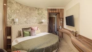 Ein Hotelzimmer mit einem großen Bett, einem an der Wand befestigten Fernseher, einem kleinen Tisch mit einer Obstschale und einer gebogenen Holzkonsole.