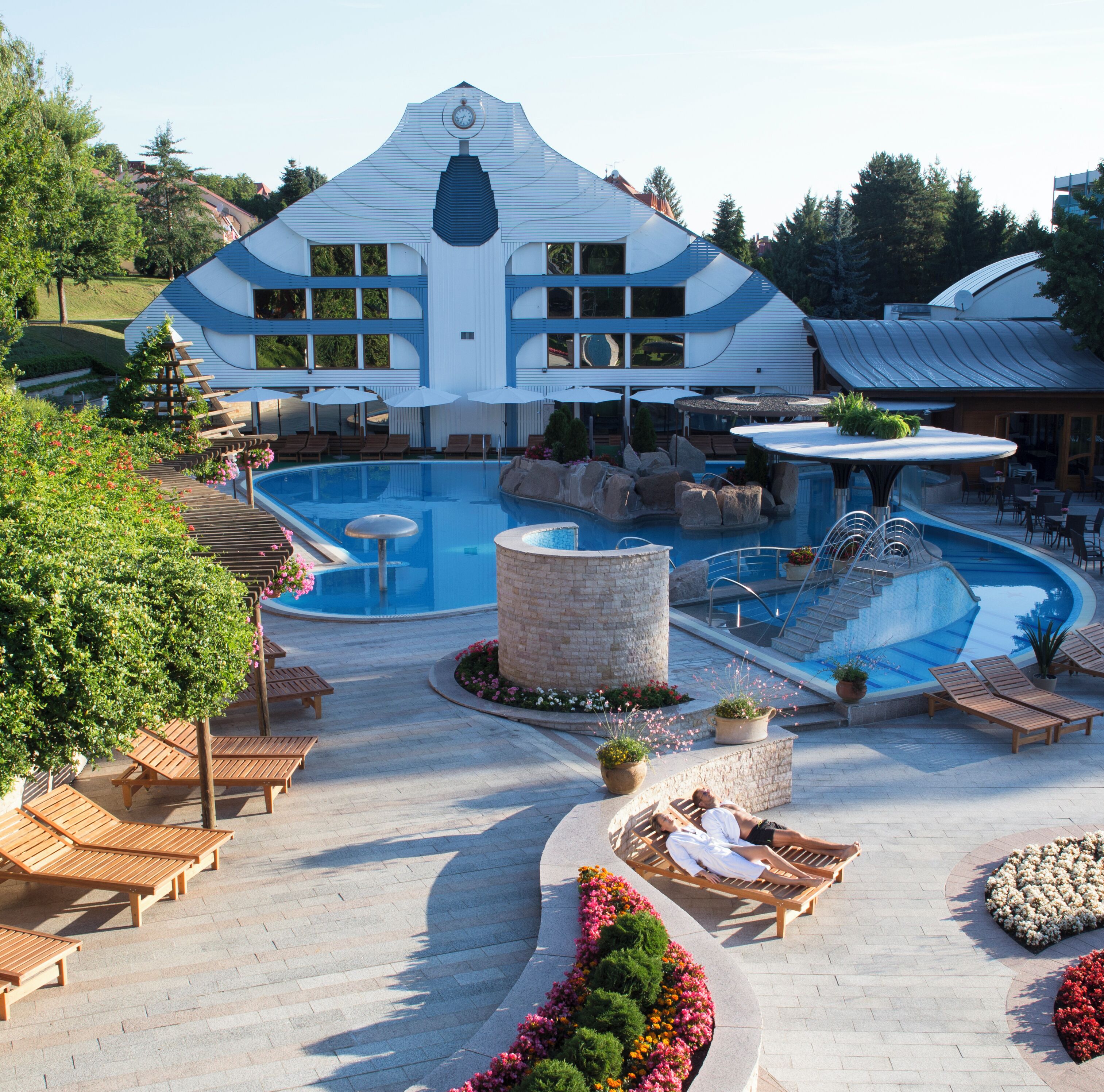 Un resort con una amplia piscina, mobiliario de exterior y un edificio distintivo con torre de reloj.