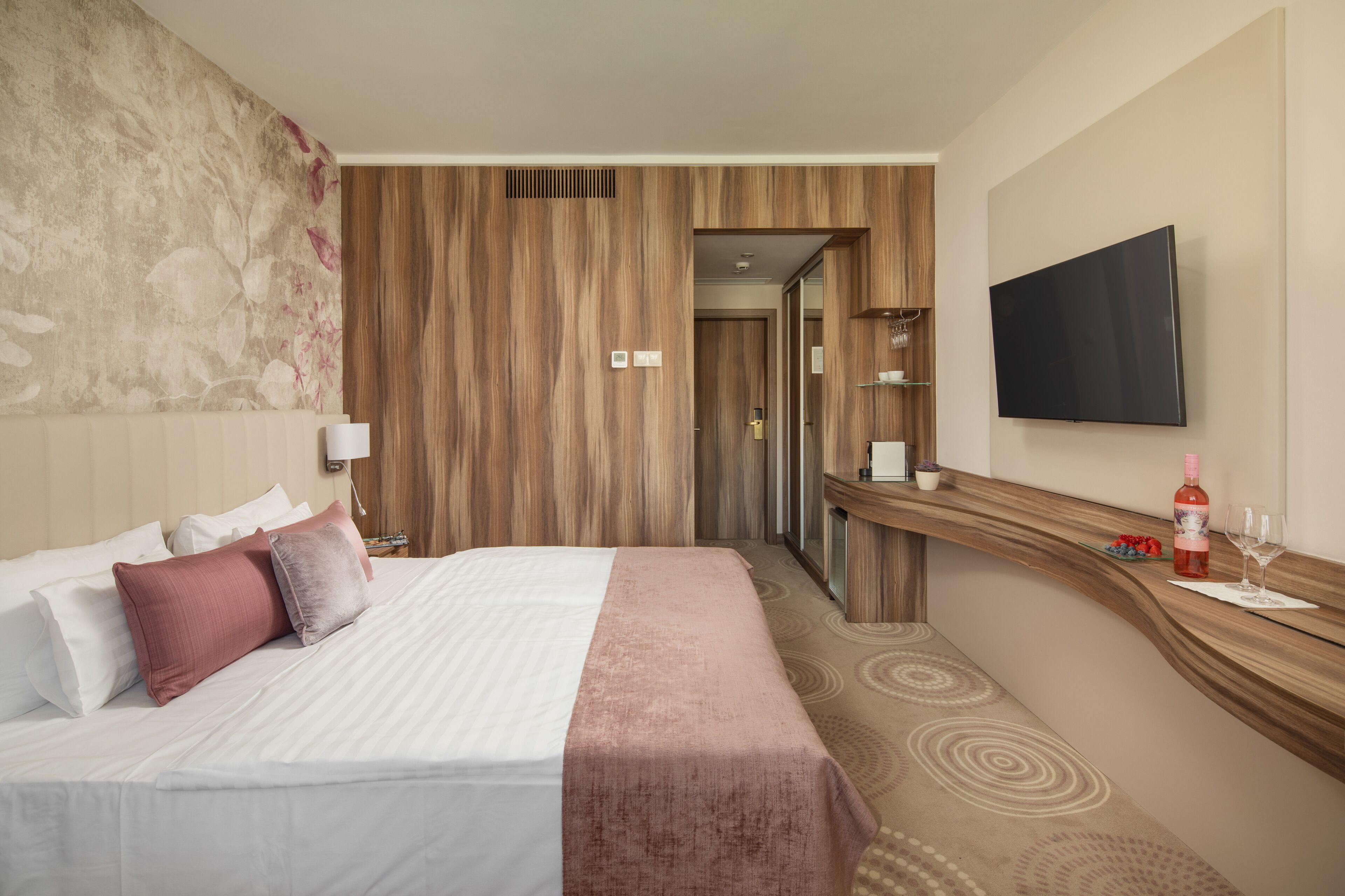 A hotel room with a bed, a TV, a wooden panel wall, and a bathroom door.