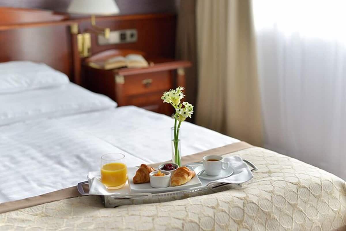 Un plateau de petit-déjeuner bien présenté, avec des croissants, du jus d’orange et du café, posé sur un lit recouvert d’une couette blanche.