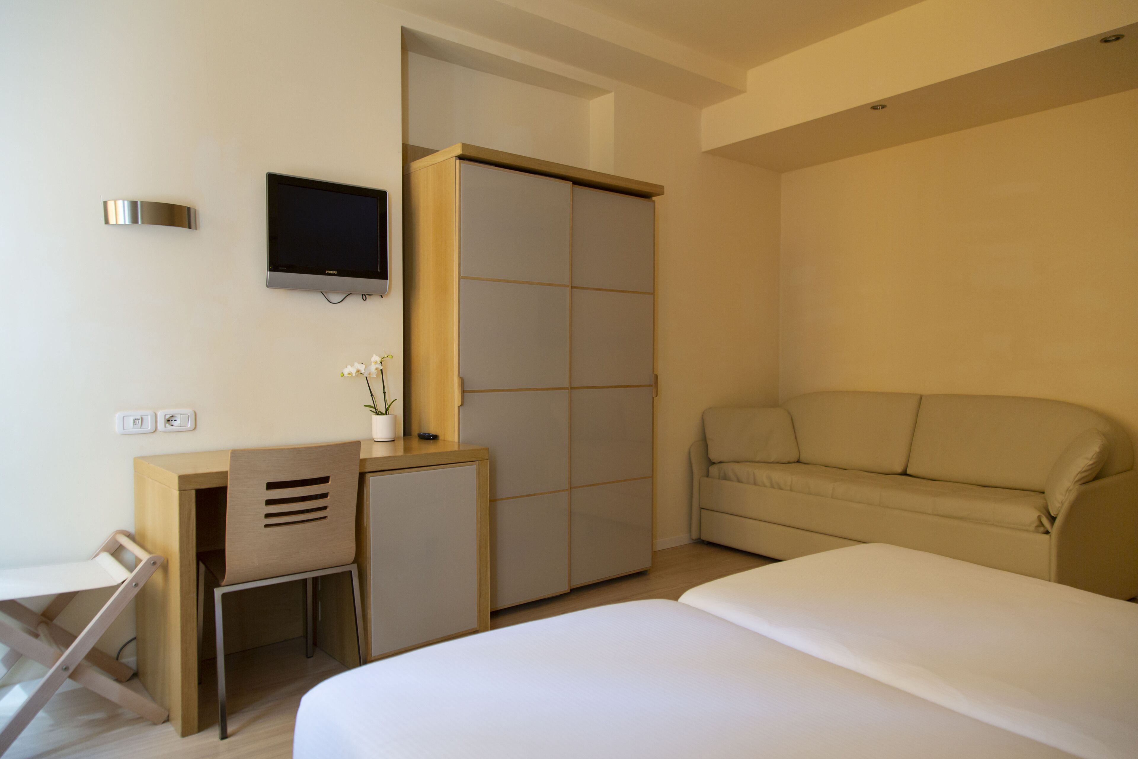 A hotel room with a bed, a desk with a chair, a television, and a wardrobe.
