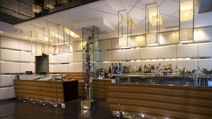 Un espace bar moderne avec un comptoir en bois, des cloisons en verre et une grande variété de bouteilles.